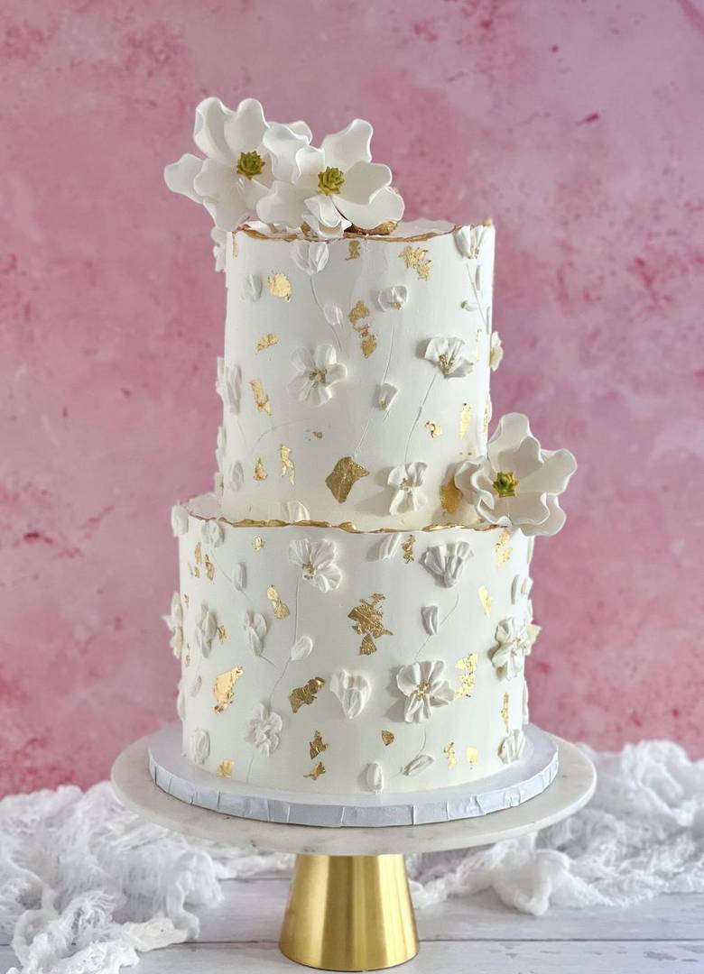 Ivory two-tier wedding cake with hand-piped blossoms and gold leaf
